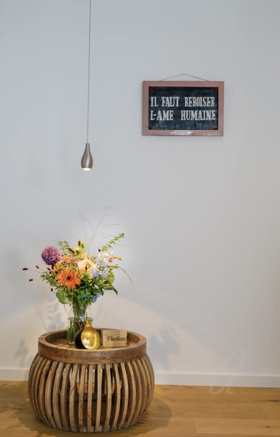 Schild an heller Wand: Il faut reboiser l'âme humaine – mit Blumenstrauß auf Holztisch